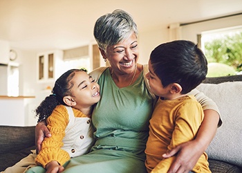 Woman wearing green sitting on a couch hugging a girl and a boy wearing yellow